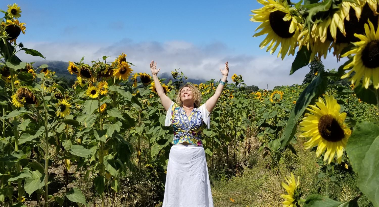 Woman with arms raised up and smiling in the sunshine in a field of large sunflowers