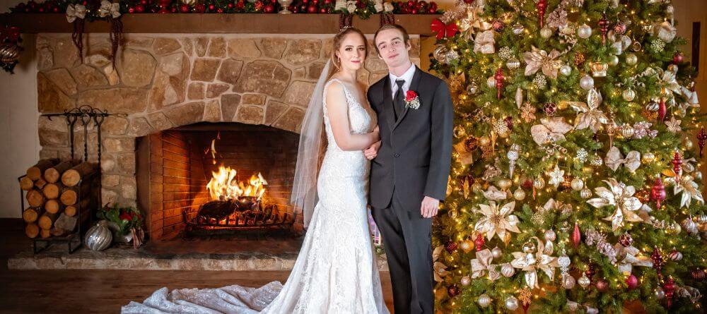 Bride and groom standing in front of a roaring fireplace and beautifully decorated Christmas tree at the Carmel Valley Lodge.