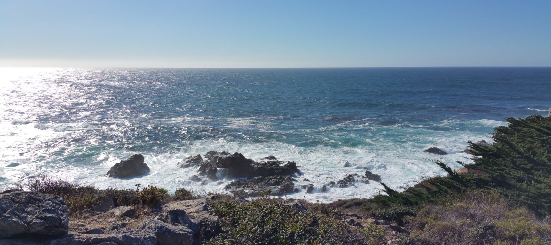 View of the ocean with waves crashing on rocks next to cliff with rocks and grasses